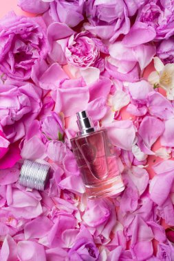 Etrafında pembe arka planda güller olan bir şişe parfüm var. romantik ve güzellik konsepti 