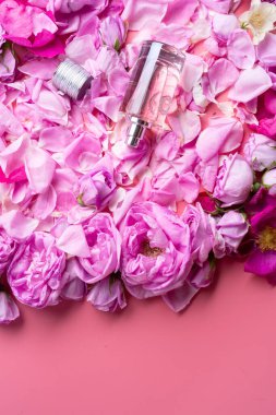 Etrafında pembe arka planda güller olan bir şişe parfüm var. romantik ve güzellik konsepti 