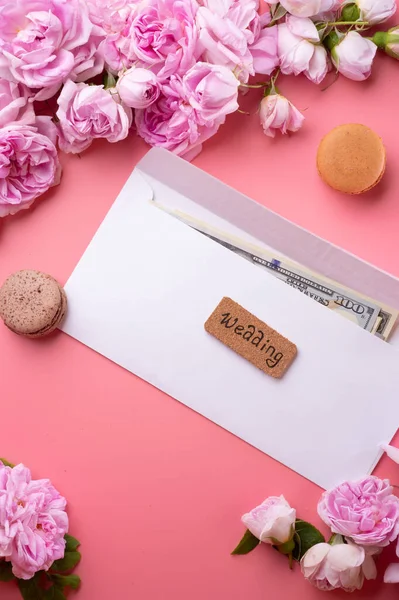 white envelope with cash around roses and macaroons against  pink background. life style concept