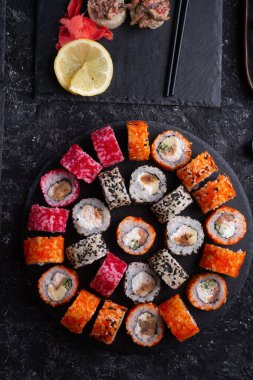 Siyah masada yükselen siyah tabakta servis edilen balık ve şitake mantarlarıyla hazırlanmış suşi ruloları. düz yat