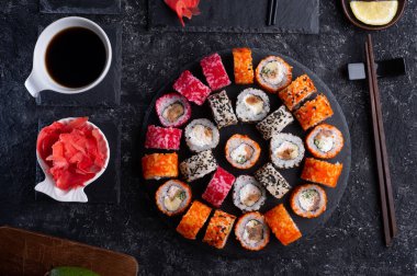 Siyah masada yükselen siyah tabakta servis edilen balık ve şitake mantarlarıyla hazırlanmış suşi ruloları. düz yat