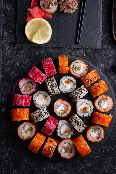 Siyah masada yükselen siyah tabakta servis edilen balık ve şitake mantarlarıyla hazırlanmış suşi ruloları. düz yat