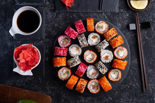 Siyah masada yükselen siyah tabakta servis edilen balık ve şitake mantarlarıyla hazırlanmış suşi ruloları. düz yat