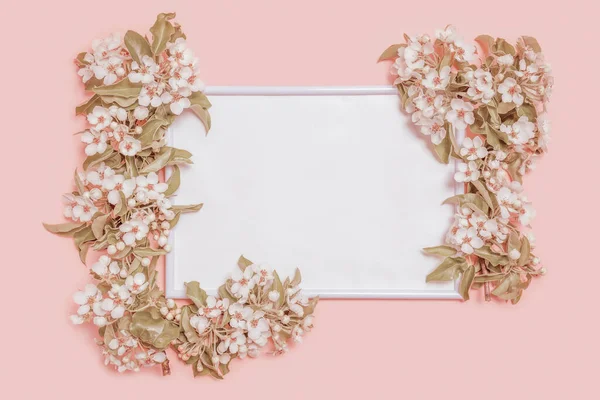 Çiçekli armut dalları ve pastel pembe arka planda fotoğraf çerçevesi olan yaratıcı bir düzen. Bahar minimum konsepti. Düz konum, kopyalama alanı, üst görünüm. Tonlama süreci