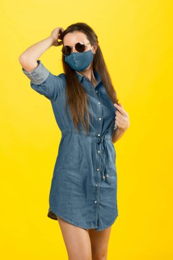Kot gömlekli ve maskeli güzel kız. Yaz için de güneş gözlüğü takıyor.