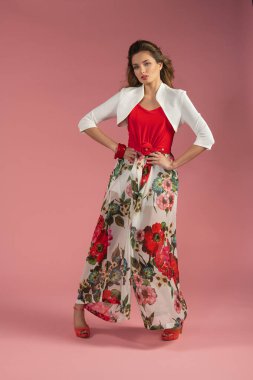 Pembe ve kırmızı çiçekli bahar çiçekli bir elbise giymiş. Moda tarzı poz veriyor. Rüzgarda saç