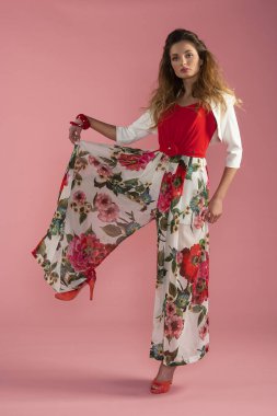 İnce kıvırcık saçlı, ipek pembeli, kırmızı elbiseli bir kadın model kameraya bakıyor. Romantik elbiseli şirin kız. Bahar konsepti.