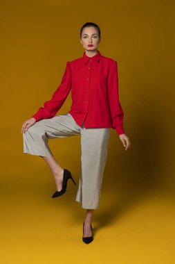 Sarı arka planda kırmızı ve gri elbiseli çekici moda kızı saç stiliyle poz veriyor. , 