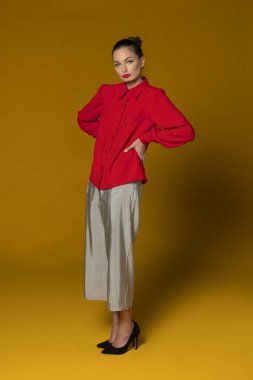 Kırmızı gömlekli, bahar elbisesi giyen, sarı arka planda poz veren çarpıcı bir manken. Kameraya bakıyor.