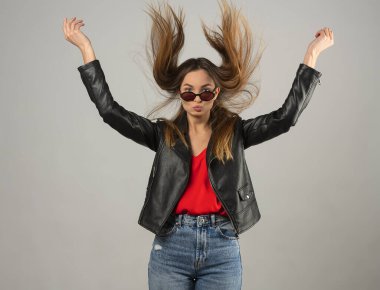 Çekici, güler yüzlü, mutlu bir kadın gri stüdyo arka planında yüzler yapıyor. Kafasında saçlar uçuşarak zıplıyor.