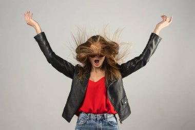 Mutlu bir manken yüzü, günlük kıyafetler, yüzünde uçuşan saçlar. Kolları havada zıplıyor.