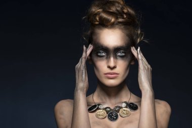 Moda yaratıcı makyaj çok koyu renkli punk, güzel model koyu mavi üzerine poz veriyor, parlak eli ve saç stili var, geri dönüşümlü malzemeden kolyesi var.