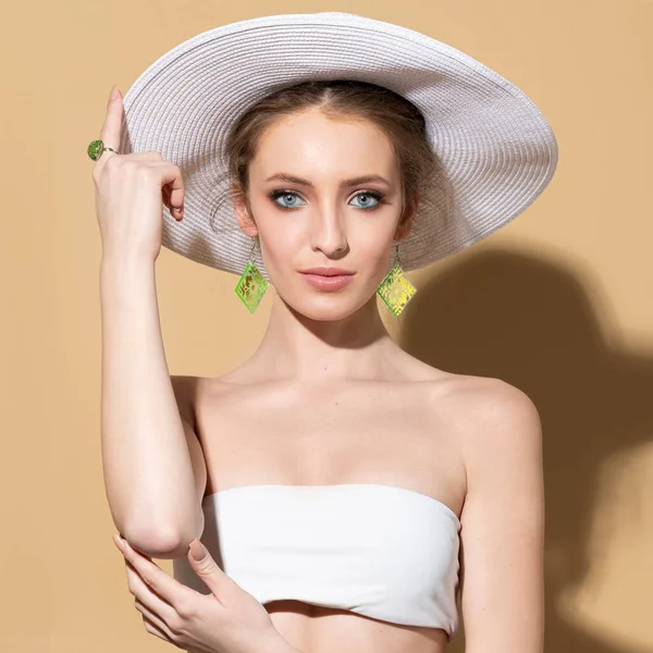 穿着夏装 头戴白帽 头戴漂亮珠宝的漂亮模特的时尚肖像 她是以米色为背景摆姿势的 — 图库照片