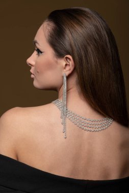 Kolyesi ve bej arkaplanda saç stili olan elmas küpeli güzel, genç bir esmer.