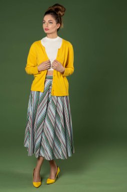 Genç bir kadın ve güzel eski tarz bir elbise giyiyor, çizgili bir elbisesi var, yeşil renkte poz veriyor ve başka tarafa bakıyor.