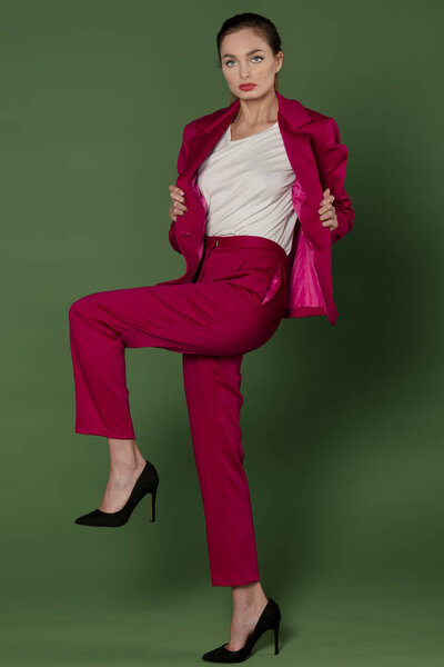very gorgeus model , posing in fashion style with a fuchsia outfit with jacket and pants , over green backgound
