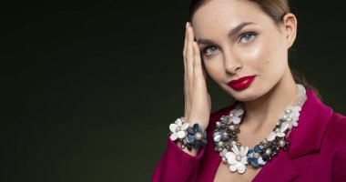 Kırmızı elbiseli, koyu sırt çantasına poz veren güzel bir kızın yakın portresi. Göz kamaştırıcı gözlerle kameraya bakıyor ve şık takılar takıyor.