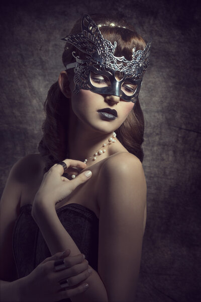 Gorgeous, mysterious female in carnival, silver mask, with brown long hair and dark make up wearing black dress.