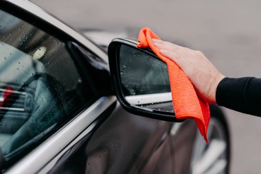 Adamların siyah arabaya mikrofiber bez ile su silmelerine yakın çekim. Dikiz aynasına odaklan. Ulaşım self servis