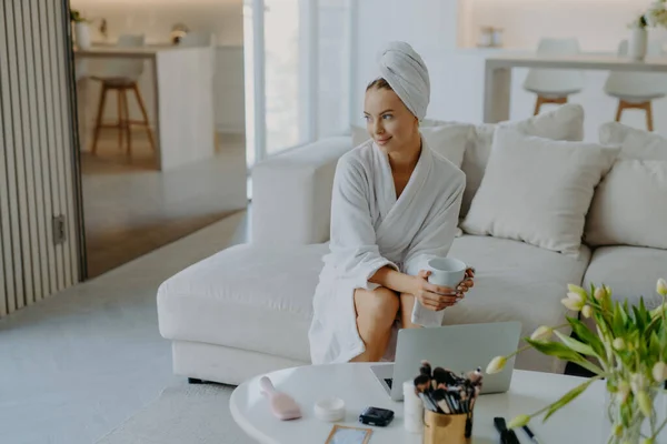 Relaxed Thoughtful Woman Dressed Bathrobe Wrapped Towel Head Sits Sofa — Stock Photo, Image