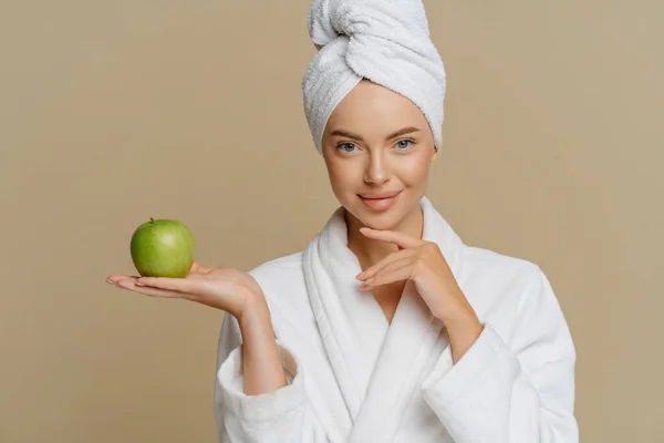 美しい健康的な女性のタッチあごは優しく緑のリンゴを保持している完璧な滑らかな肌は 新鮮な果物と屋内モデルの頭の上に柔らかい白い国内のローブとラップタオルを身に着けています 皮膚治療 — ストック写真