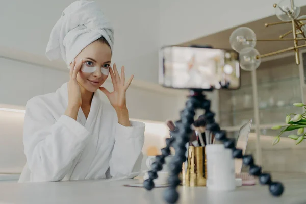Vlog 'u için cilt bakımı videosu kaydederken kozmetik yamalar kullanan bornozlu kadın güzellik blogcusu — Stok fotoğraf