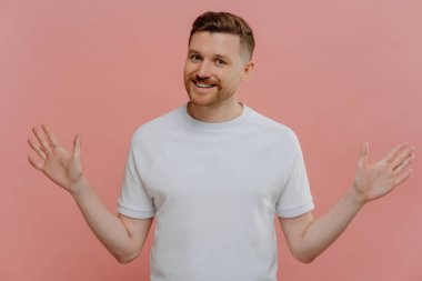 Pembe stüdyo geçmişine karşı poz verirken ellerini yana doğru açan mutlu genç adam.