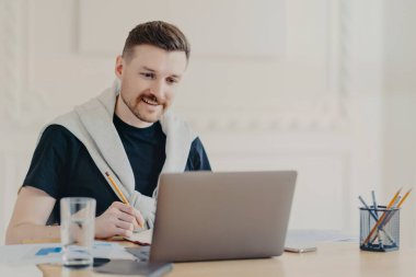 Video çağrısı sırasında not alan pozitif genç serbest yazar