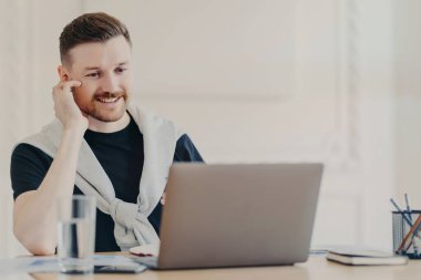 Gülümseyen erkek ofis çalışanı dizüstü bilgisayarında video görüşmesi yapıyor.