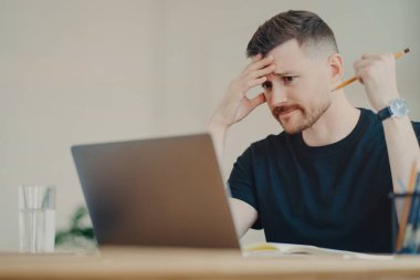 Stresli erkek ofis çalışanı endişeli yüz ifadesiyle dizüstü bilgisayara bakıyor.