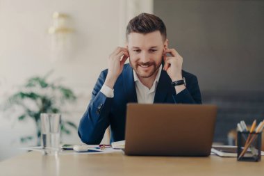 İnternet konferansı düzenleyen çekici iş adamı, dizüstü bilgisayar ve kulaklık kullanıyor.