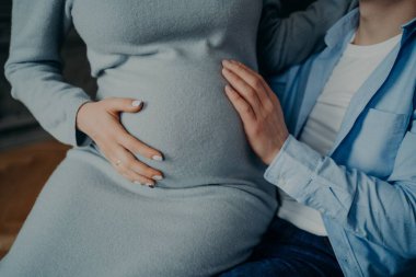 Hamilelik ve aile kavramı. Hamile kadının göbeğine dokunduğu kesikli çekim, kocasının ellerinde bebek pozu bekliyor. Erkek, karısının karnına dokunur.