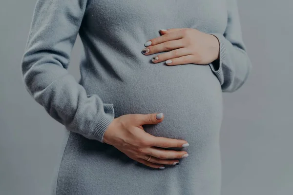 Unrecognizable pregnant woman touches belly wears dress anticipates for baby. Pregnancy maternity expectations concept. Cropped shot. — Stock Photo, Image