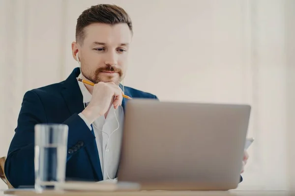 Executive manager in auricolari guardando il computer portatile mentre si lavora in ufficio — Foto Stock