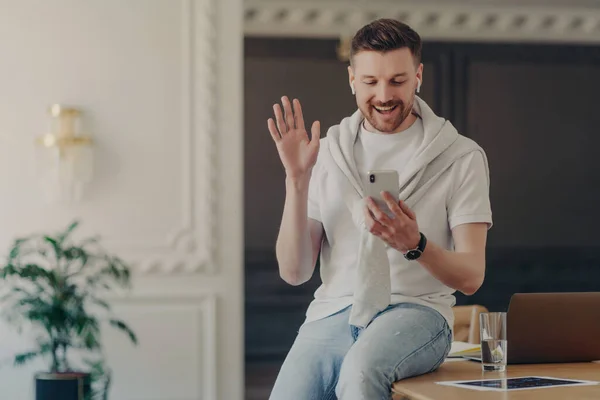 Freelancer masculino excitado com videochamada no celular sentado na mesa de trabalho Imagens De Bancos De Imagens Sem Royalties