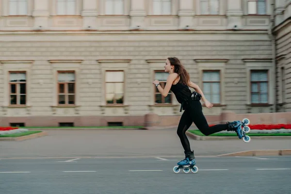 Wanita muda yang sehat memiliki sosok yang ramping yang pas menyebabkan gaya hidup aktif menghabiskan waktu luang di luar wahana pada rollerblade berpose sendiri di udara terbuka terhadap latar belakang bangunan — Stok Foto