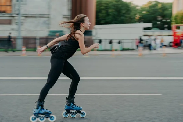 Full length shot of young slim woman rollerblades along asphalt on street enjoys speed spends free time on favorite hobby poses outdoors breathes fresh air. Rollerskating — Stock Photo, Image