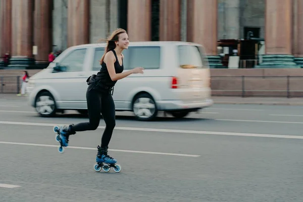 Mulher sorridente feliz passa o tempo de forma ativa passeios em rolos de patinação demonstrou alta velocidade durante poses movimento em roaad com transporte em segundo plano. Passatempo e estilo de vida. — Fotografia de Stock