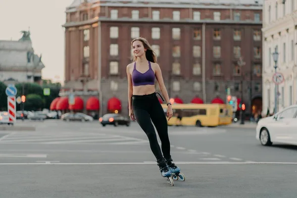 Donna magra sportiva in attiva usura cavalca su lame gode di attività di fitness all'aperto durante la calda giornata estiva posa in luogo urbano su asfalto. Rollerblade e concetto di svago — Foto Stock