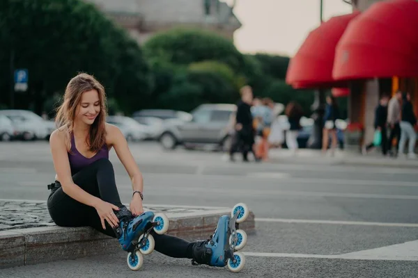 Die sympathische dunkelhaarige Europäerin zieht Inlineskates an und posiert auf Inlineskates vor verschwommenem Stadthintergrund, hält sich fit und verbringt ihre Freizeit aktiv. Außenschuss — Stockfoto