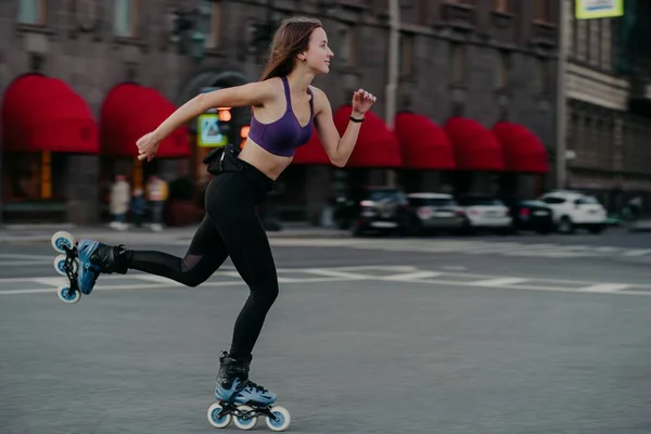 Slim jeune femme monte rapidement sur patins à roulettes améliore l'agilité de l'équilibre et la coordination habillée en haut et leggings recadrés pose sur la route de la rue focalisée sur la distance — Photo