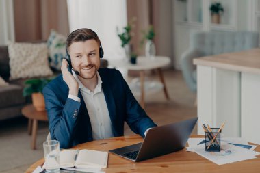 Smiling handsome young businessman in headset studying online at home