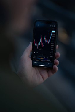 Akıllı telefon ekranında borsa verilerine bakan ve Forex grafiğini analiz eden bir işadamı.