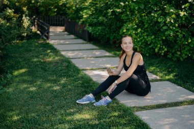 Aktif esmer Avrupalı kadının dışarıda aktif eğitim için akıllı telefondan müzik indirdiği açık hava çekimi, aktif giysi paylaşımı içeriği blog içeriğiyle yapılan antremandan sonra mutlu bir şekilde uzaklaştı