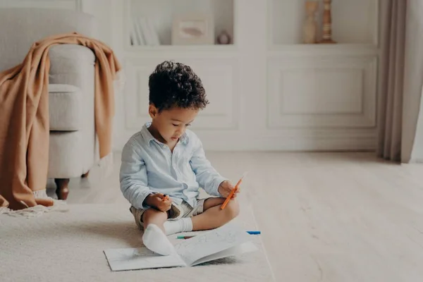 Маленький кучерявий хлопчик з мулатками з розфарбованою книгою вдома — стокове фото