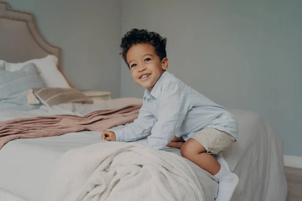 Маленький афроамериканець, що бавиться на великому ліжку вдома. — стокове фото