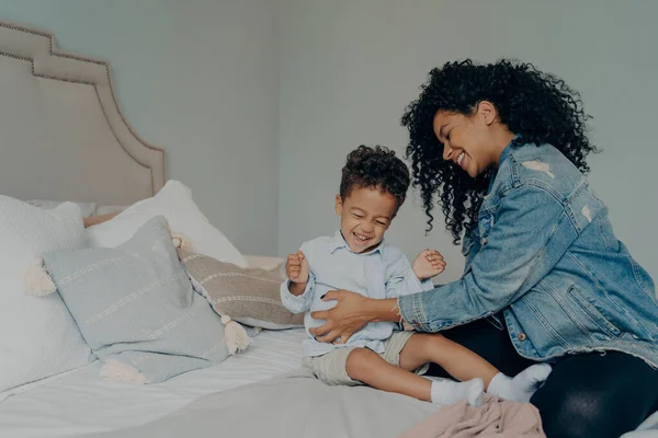 Amar afro-americana madre cosquillas hijo mientras se divierten juntos en el dormitorio — Foto de Stock