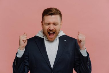 Neşeli adam yumruklarını sallıyor ve mutluluktan bağırıyor, başarıyı kutluyor.