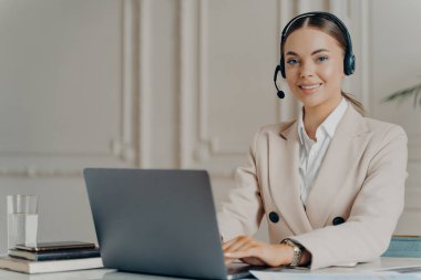 Kamera karşısında gülümseyen kulaklık takan arkadaş canlısı müşteri destek operatörü.