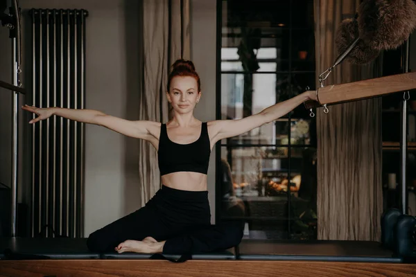 Pilates instruktur duduk di atas meja trapeze dengan lengan terentang ke kedua sisi — Stok Foto